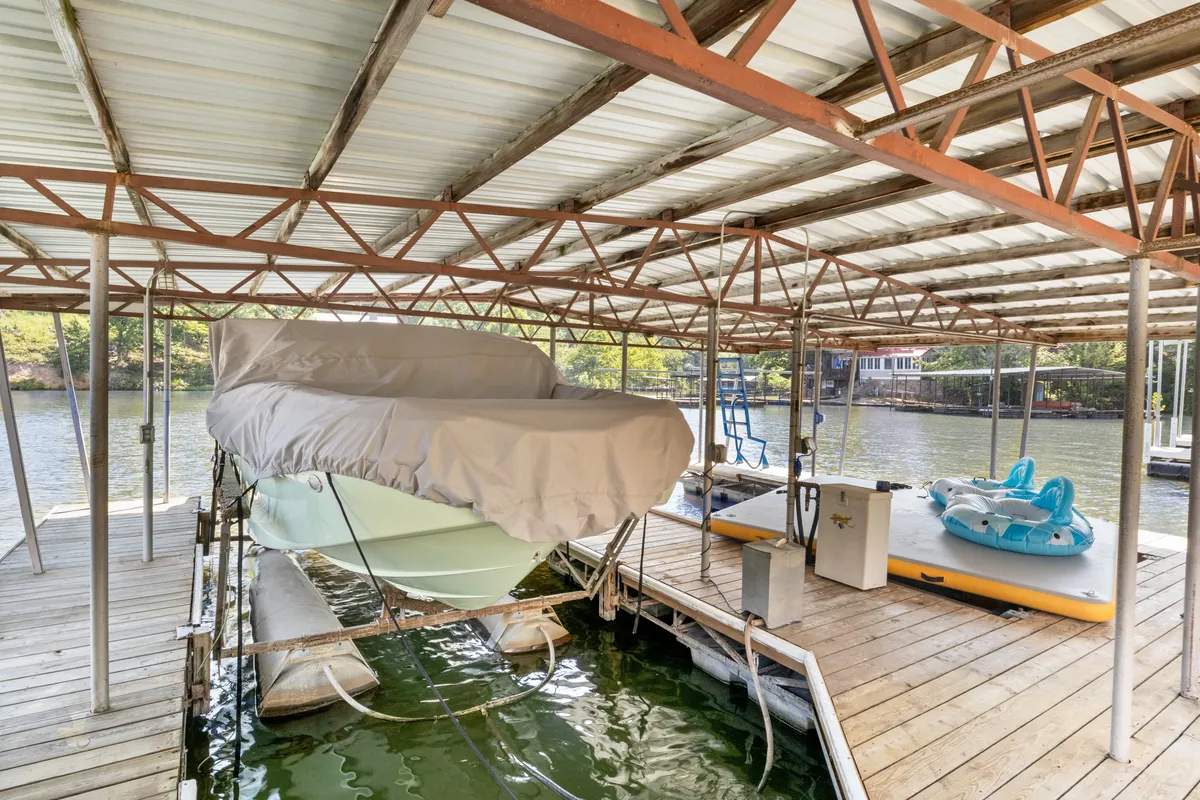 This image features a covered boat, a paddleboard, a kayak, and a dock structure at the water's edge, evoking a sense of leisurely waterfront adventure. The calm water and inviting equipment suggest opportunities for boating, fishing, and water sports right from the dock.