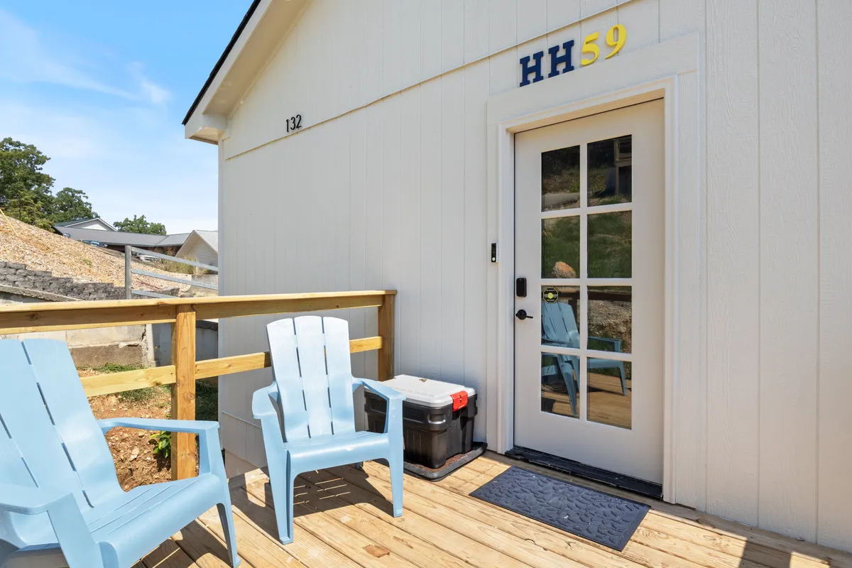 The front exterior of the home showcases blue Adirondack chairs arranged by the entrance, creating an inviting and welcoming first impression. The glass-paneled front door and numbered address add a touch of personalization and exclusivity, while the outdoor setting hints at the quiet, private cove location.