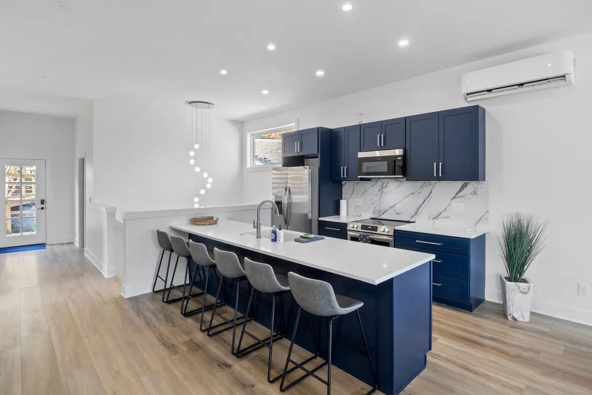 A chic kitchen scene with an elegant island that features comfortable seating, a suite of stainless steel appliances, a marble backsplash, and pendant lighting. The space feels open and ready for gatherings or casual meals.