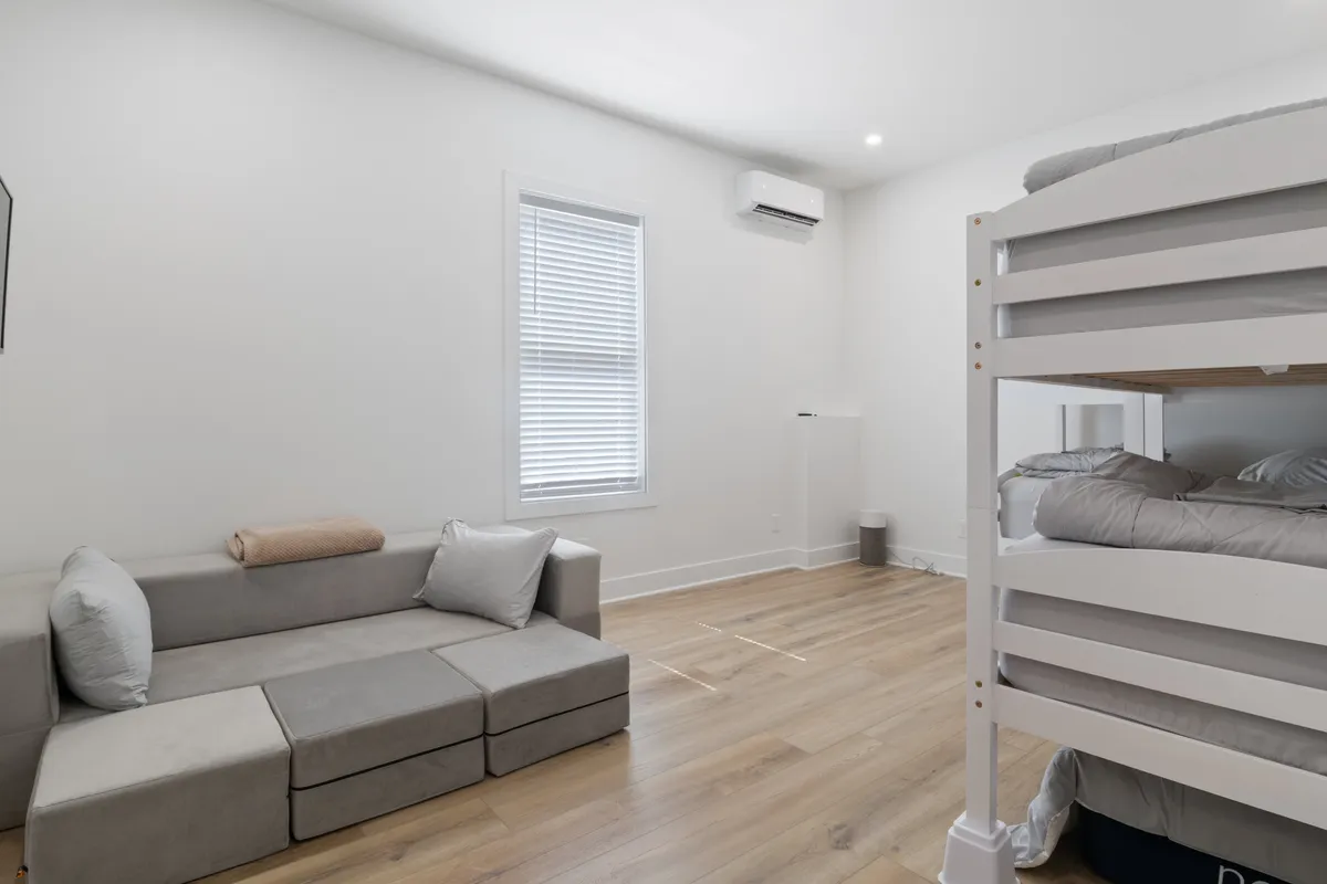 A dedicated bunk room with a bunk bed, a modular sofa for lounging, and a large window for ample natural light. The space is playful and inviting, ideal for kids or extra guests to relax, read, or enjoy games together.
