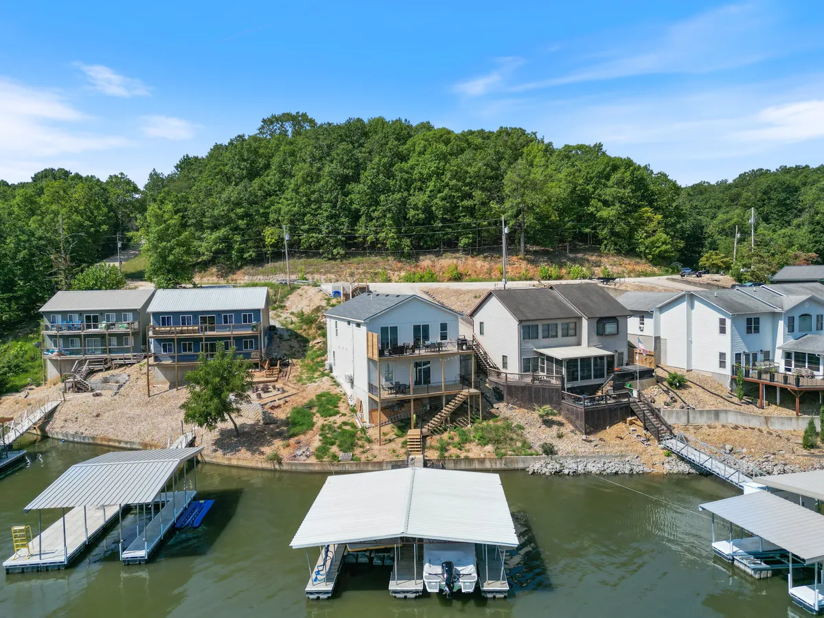 A relaxed exterior scene showing waterfront houses, a dock with boats, and a green hillside. The area appears calm and welcoming, ideal for both water activities and gathering with friends or family after a day outdoors.