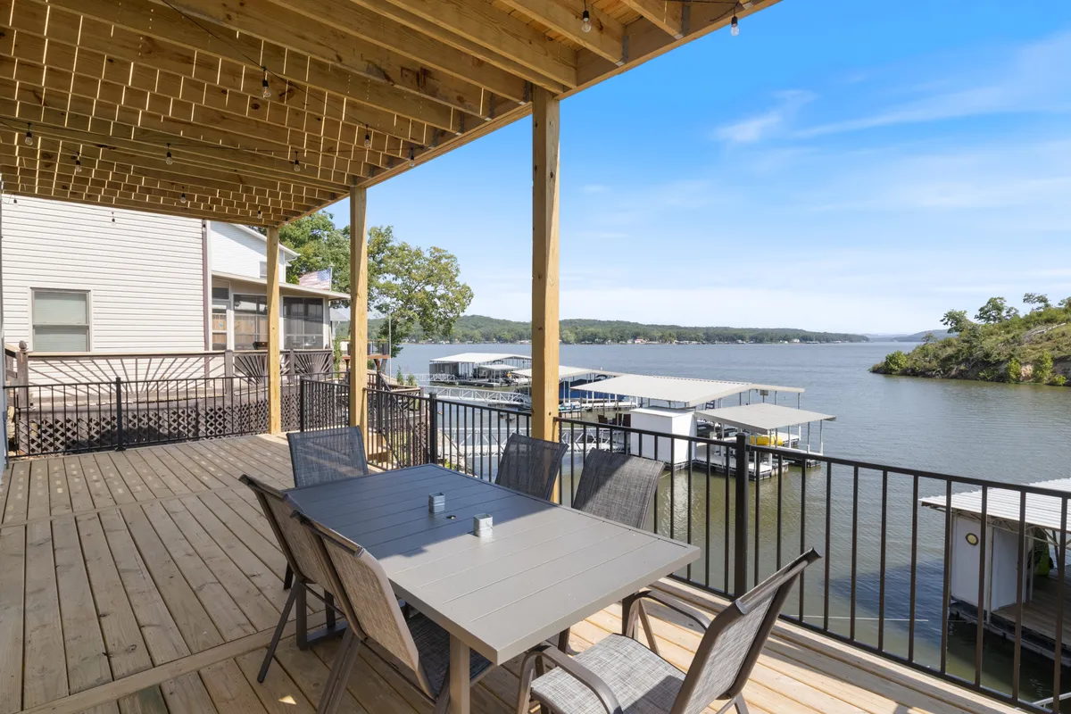 This image features a spacious deck area overlooking the water, furnished with a dining table and chairs, and with visible boat docks just beyond. The deck is perfectly set up for outdoor dining, social gatherings, and offers a serene water view, embodying the concept of lakeside leisure.