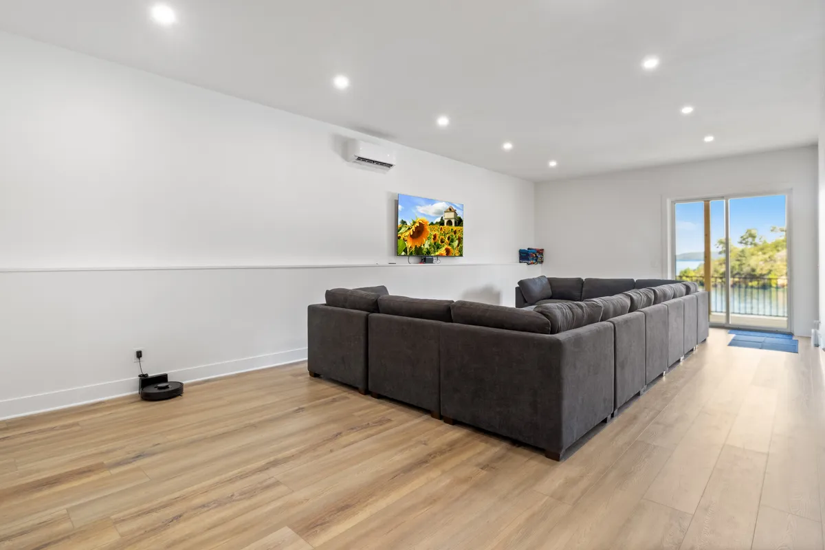 This scene centers on a large sectional sofa oriented towards a wall-mounted television, with sliding glass doors providing a seamless transition from the interior to the outdoors. The ample seating and direct view to nature highlight the lounge’s dual focus on comfort and views.