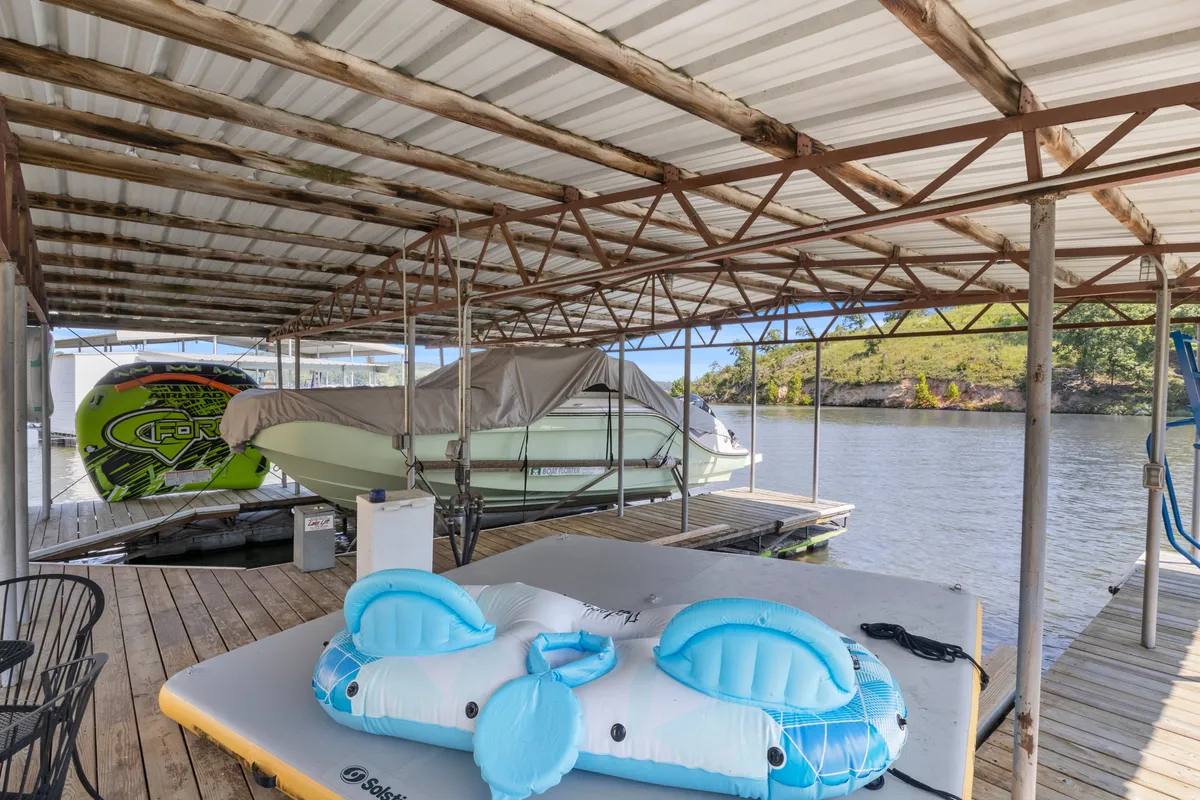 A vibrant scene showing boats moored at the dock, a floating mat on the water, and the dock structure itself. The setting is lively and inviting, evoking images of swimming, sunbathing, boating, and sharing fun lake days with friends and family.