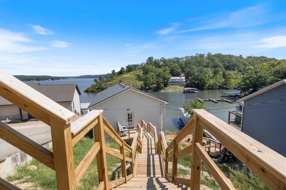 A scenic view looking down a wooden staircase toward a tranquil lake, with greenery and homes lining the water. The landscape is inviting and peaceful, perfect for hiking, wildlife spotting, and enjoying natural beauty.